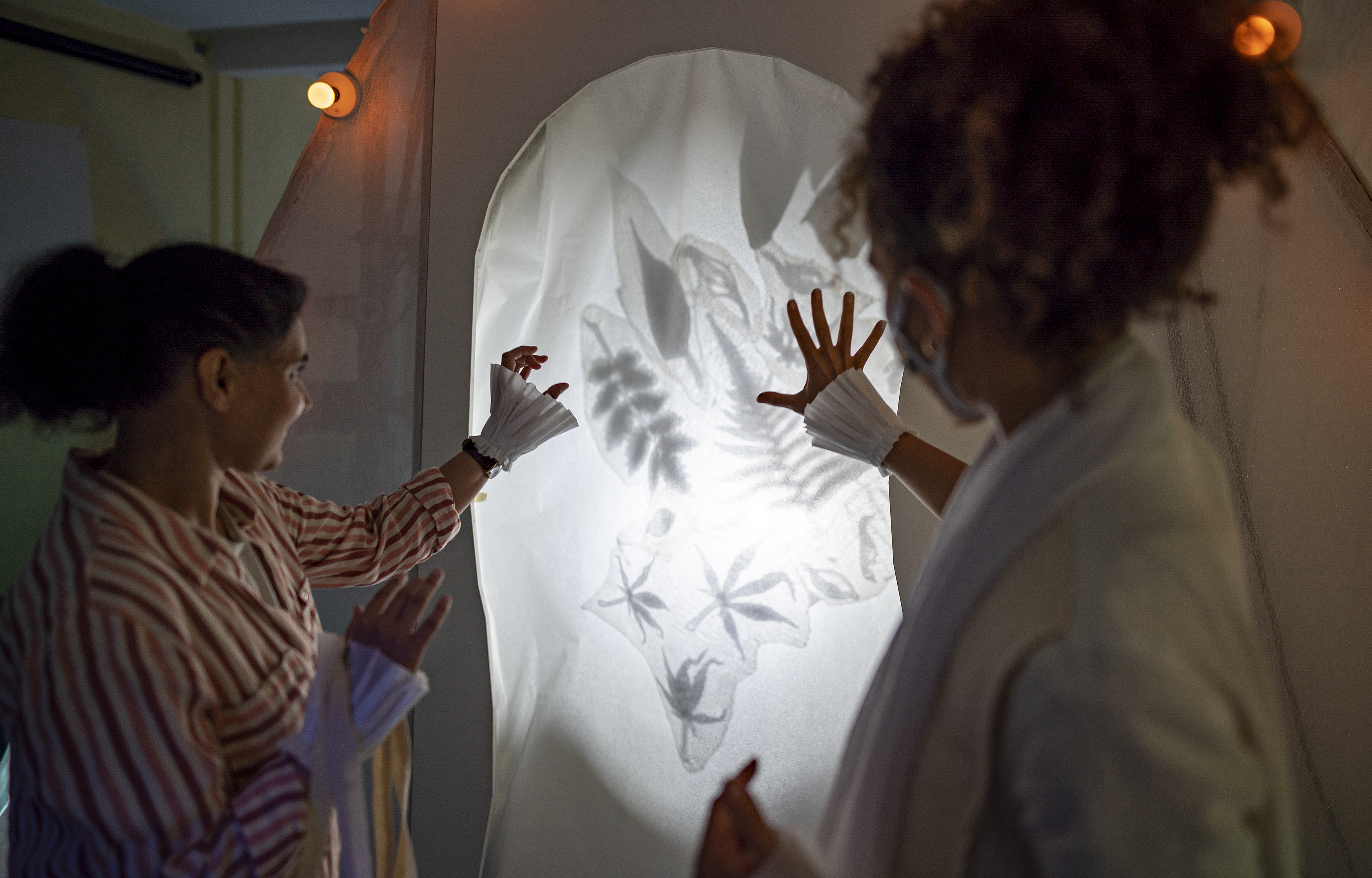 A performer encourages a participant to touch a lit up wall with various lead shadows.